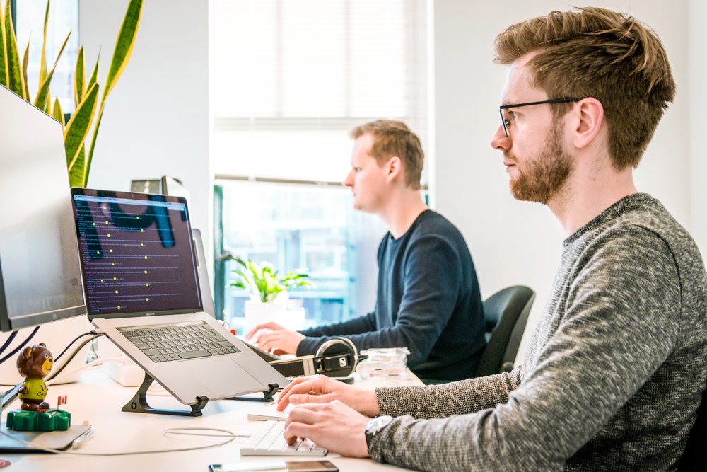 Two developers working side by side, code on the laptop screen